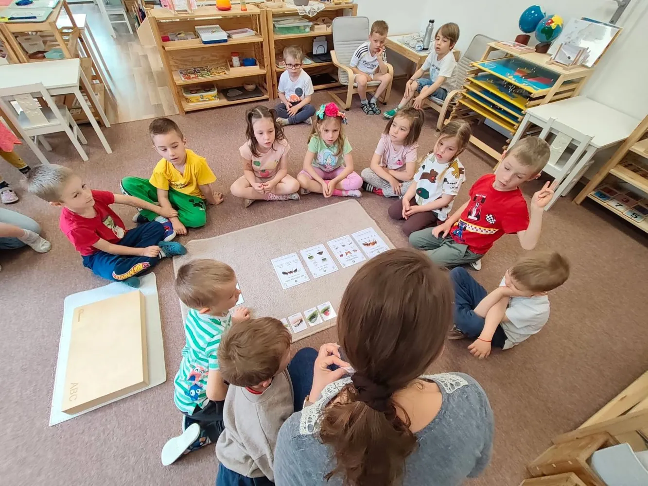 Deti a sprievodkyňa v spoločnom kruhu na koberci v Montessori prostredí